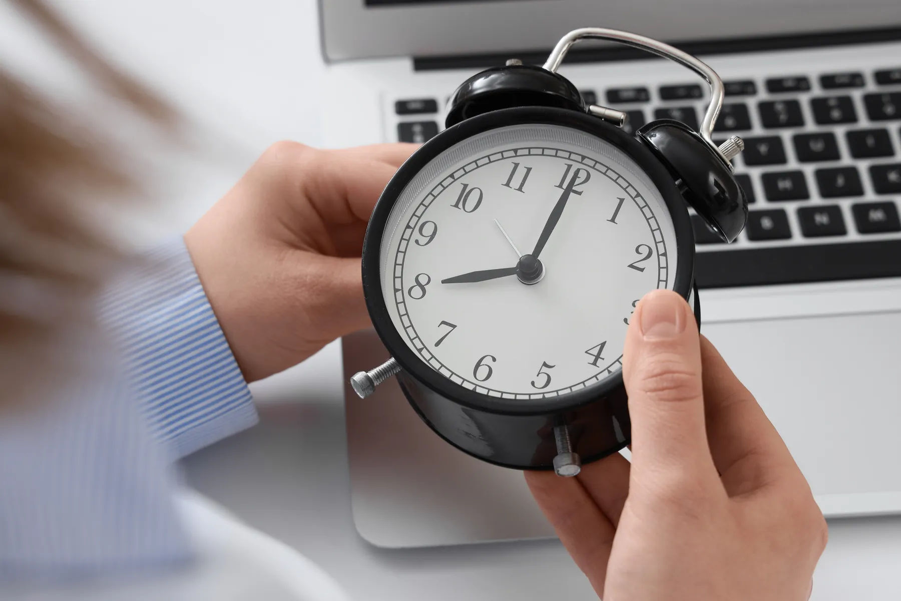 A hand holding an alarm clock in front of a laptop
